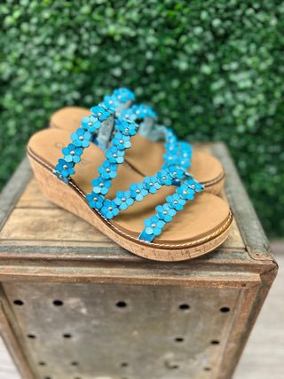 Corky's wedge sandals with decorative flower embellishments on straps, displayed on wooden crate outdoors.