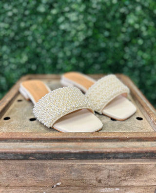 Corky's Our Lil Secret pearl-embellished slide sandals displayed on wooden surface with greenery background