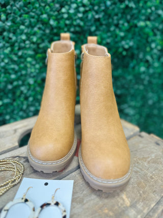 Tan leather ankle boots with chunky soles displayed on wooden surface with green foliage background