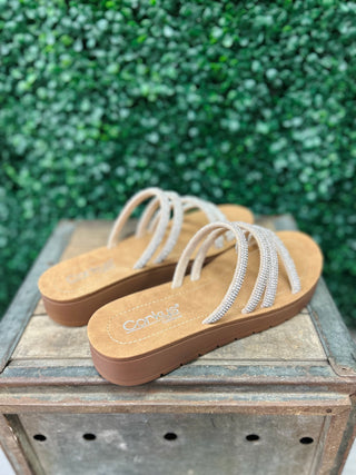 Corky's strappy rhinestone sandals with embellished straps on wooden surface against green foliage background