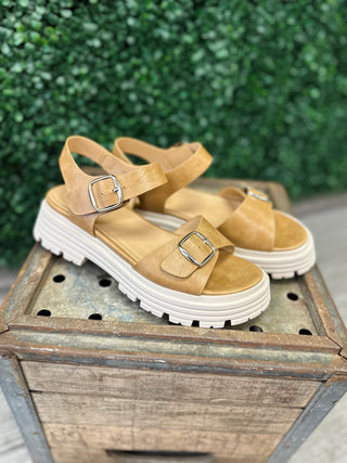 Caramel leather platform sandals with buckle straps and white chunky sole on wooden crate