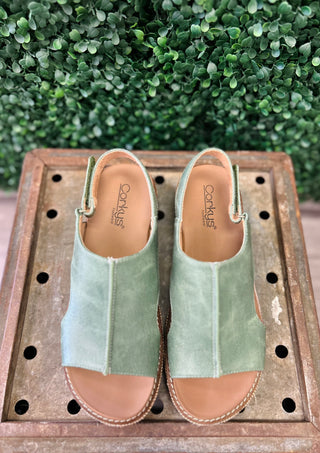 Corky's Volta wedge sandals in green suede with ankle strap displayed on wooden surface