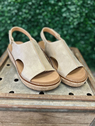 Gold metallic sling-back wedge sandals with platform soles displayed on weathered wooden surface outdoors.