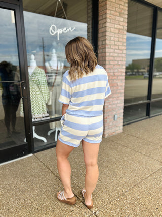 Woman wearing a matching striped short sleeve top and shorts set with sandals outside boutique.