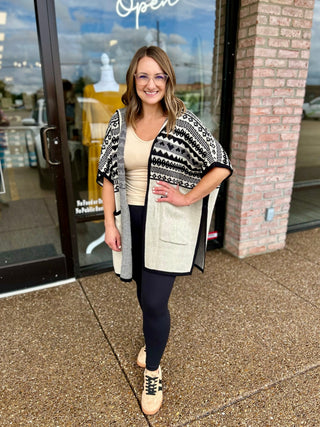 Woman wearing a patterned knit wrap cardigan with geometric design, posed outside a boutique storefront.