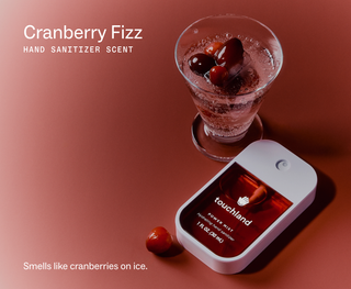 Touchland Power Mist hand sanitizer beside a fizzy cranberry drink with fresh cranberries on ice.