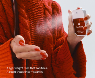 Person in red sweater spraying Touchland Power Mist hydrating hand sanitizer into their palm.