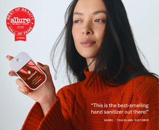 Woman in red sweater holding Touchland Power Mist Hand Sanitizer, Allure Best of Beauty Hall of Fame winner.