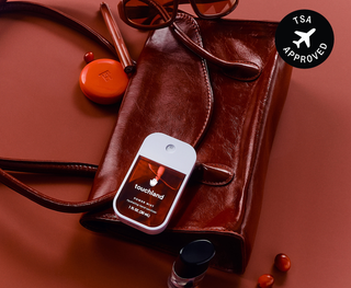 Touchland Power Mist hand sanitizer resting on a brown leather bag with accessories nearby.