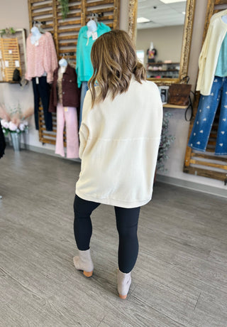 Woman wearing cream oversized tunic sweater with dark leggings and boots in clothing boutique