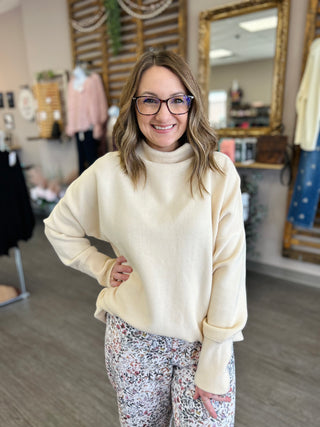 Woman wearing cream colored turtleneck tunic sweater with floral leggings in clothing boutique setting