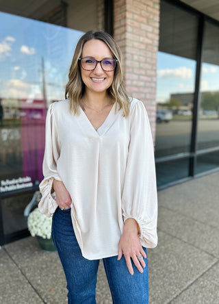 Woman wearing cream balloon sleeve blouse with jeans, smiling outdoors in front of storefront