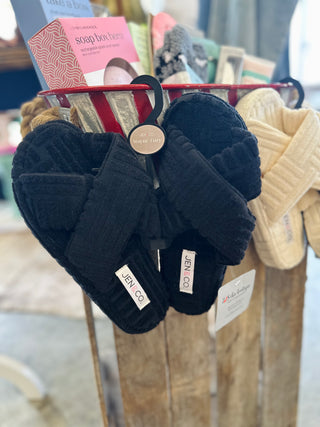 Black criss-cross fuzzy slippers hanging on display rack with brand tags in retail store