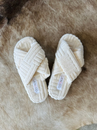 Cream colored crisscross slippers with textured fabric straps on furry background