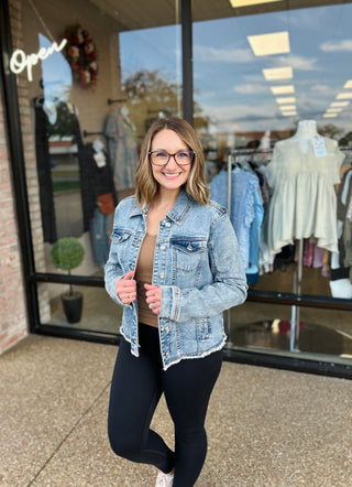Woman wearing light blue denim jacket standing outside clothing store storefront with glass windows