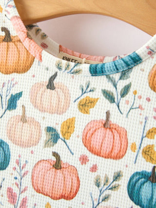 Close-up of a white waffle-knit girls' dress featuring colorful pumpkin and autumn leaves print.
