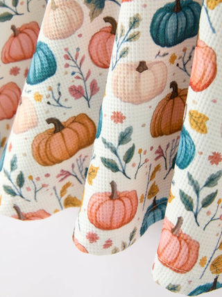 Close-up of a girls' dress featuring colorful pumpkins, autumn leaves, and floral botanical prints.