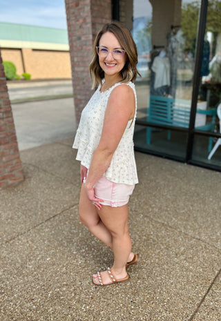 Woman wearing white tiered sleeveless tank top with floral print, styled with pink shorts and sandals.