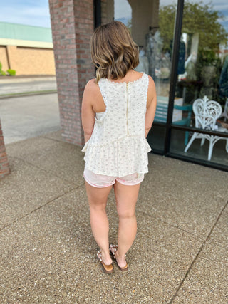 Woman wearing white tiered tank top with floral pattern and pink shorts, shown from behind.