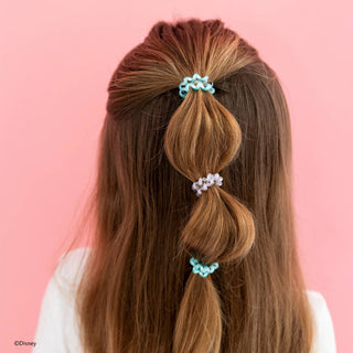 Back view of woman wearing multiple small hair ties in segmented ponytail hairstyle against pink background.