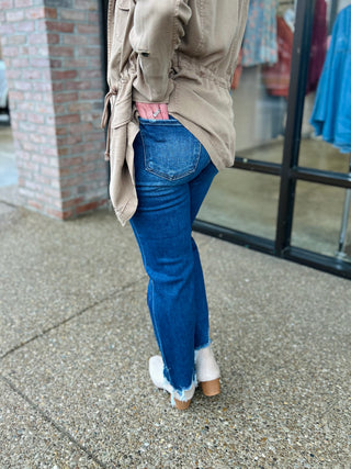 Woman wearing high-rise cropped straight leg jeans with distressed hem and beige jacket from behind.