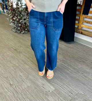 Person wearing dark blue wide leg jeans with ribbed sweater and sandals, standing indoors.