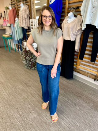 Woman wearing dark blue wide leg jeans with beige sleeveless top in clothing store