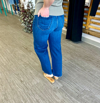 Person wearing dark blue wide leg jeans with frayed hem and brown sandals in retail store setting.