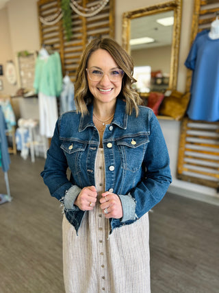 Woman wearing denim jacket over striped dress in clothing boutique store setting