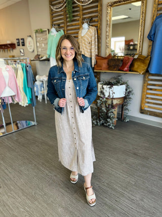 Woman wearing Dark Tide Denim Jacket over striped dress in boutique setting with clothing racks and mirrors.