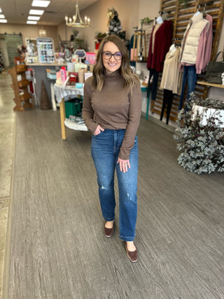 Woman wearing dark wash distressed cropped straight jeans with brown turtleneck in clothing boutique store