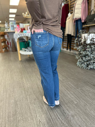 Woman wearing dark wash distressed cropped straight leg jeans with brown top in retail store setting