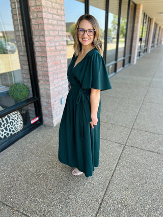 Woman wearing a green flutter sleeve wrap midi dress standing on sidewalk outside storefront