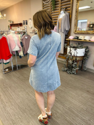 Woman wearing light blue denim dress with short sleeves in boutique clothing store setting