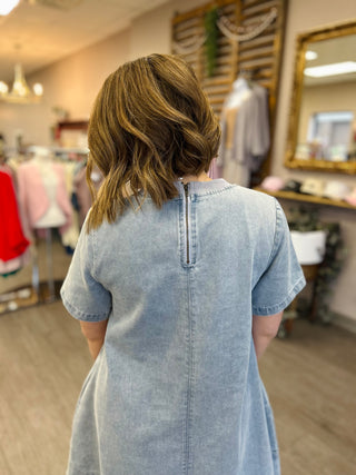 Woman wearing light blue denim dress with back zipper in clothing store setting