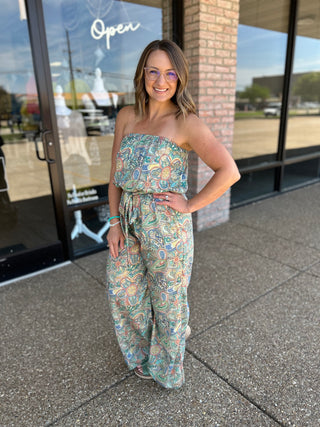 Woman wearing strapless paisley jumpsuit with colorful bohemian print, standing outside storefront.