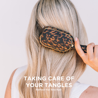 Woman brushing blonde hair with tortoiseshell detangling brush against white background