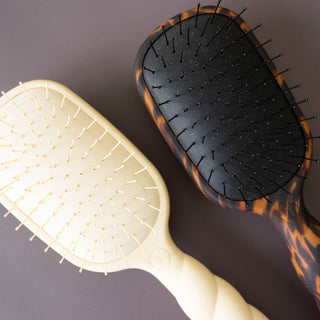 Two detangler hair brushes with flexible bristles, one in light color and one in tortoiseshell pattern.