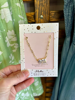 Hand holding Treasure Jewels Double Harmony Necklace packaging with gold chain and crystal pendant displayed