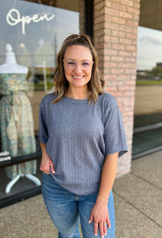 Woman wearing a relaxed ribbed short sleeve top paired with jeans, smiling outside boutique.