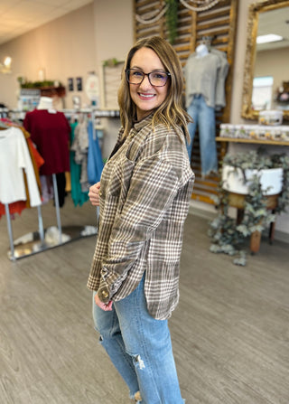 Woman wearing brown plaid button-up shacket with jeans in clothing boutique store setting.