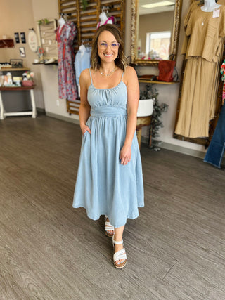 Woman wearing light blue denim midi dress with thin straps in clothing boutique setting