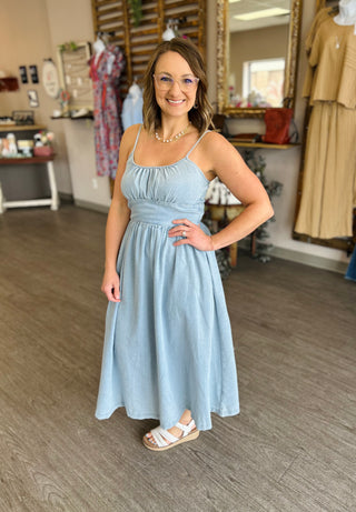 Woman wearing light blue denim midi dress with spaghetti straps in clothing boutique setting
