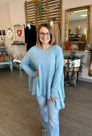 Woman wearing light blue oversized long-sleeve top in boutique clothing store setting