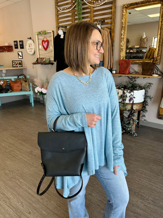 Woman wearing light blue flowing top with black crossbody bag in boutique store setting