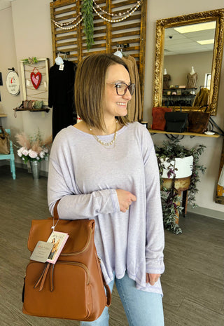 Woman wearing relaxed lavender long-sleeve top with jeans and brown handbag in boutique setting