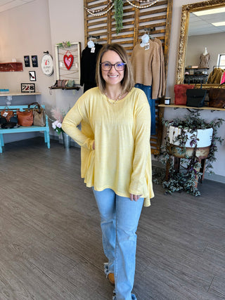 Woman wearing yellow flowy top with jeans standing in boutique store surrounded by clothing displays