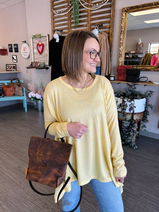 Woman wearing yellow long-sleeve top with brown leather crossbody bag in boutique setting