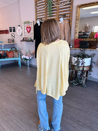 Woman wearing yellow flowing cardigan top with blue jeans in boutique clothing store setting