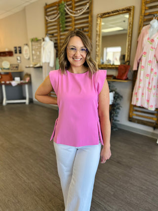 Woman wearing bright pink sleeveless top with white pants in clothing boutique store setting